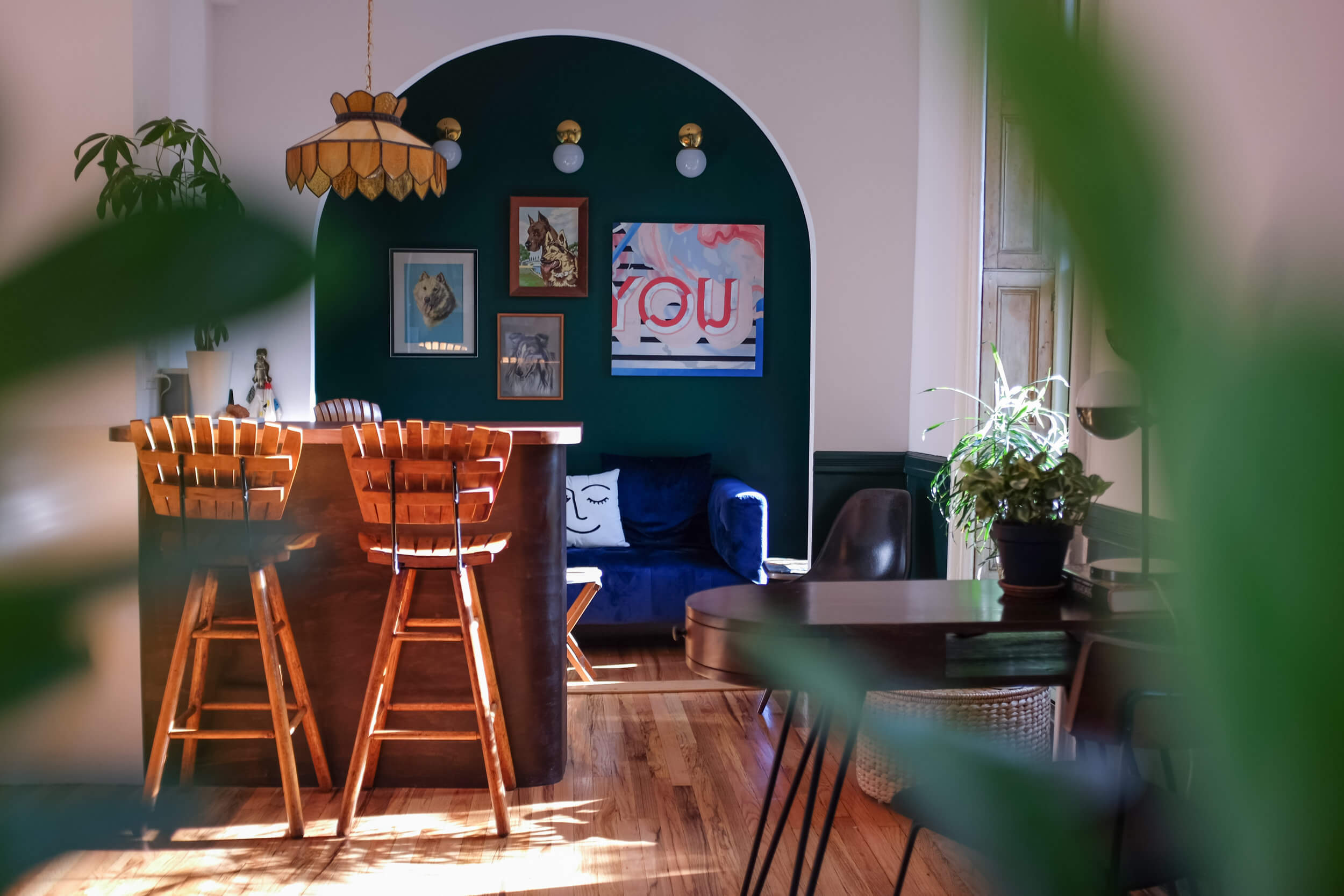 Two Arthur Umanoff bar stools at a small bar with an archway in the background that leads to a room with a blue velvet couch