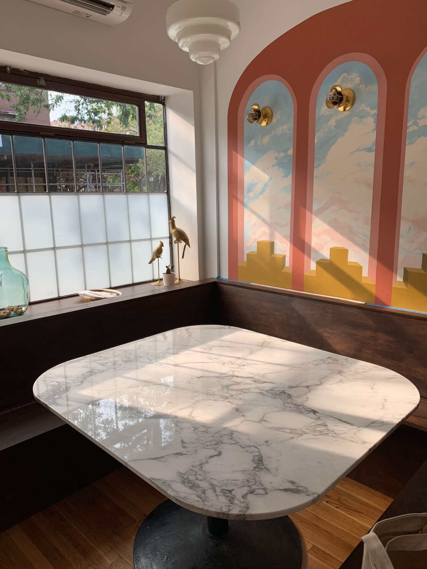 A marble kitchen table lit by a large window with walnut booth seating and a hand-painted mural